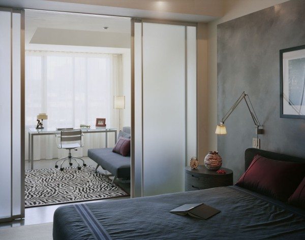 Фото спальни-кабинета, которая поделена с помощью стеклянной перегородки.