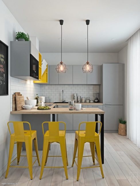 Из освещения — два подвесных потолочных светильника над барной стойкой. Кухонный гарнитур серого оттенка, выполненный в стиле минимализм.